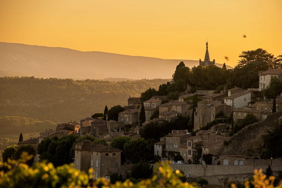 Vue rapprochée du village perché de Bonnieux au coucher du soleil, avec des maisons en pierre et une église dominant la colline.